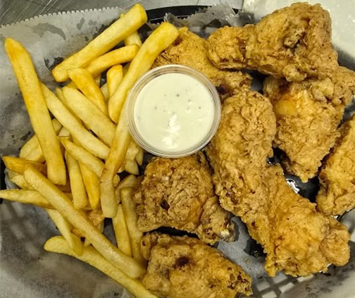 A basket of fried chicken and french fries with a cup of ranch dressing